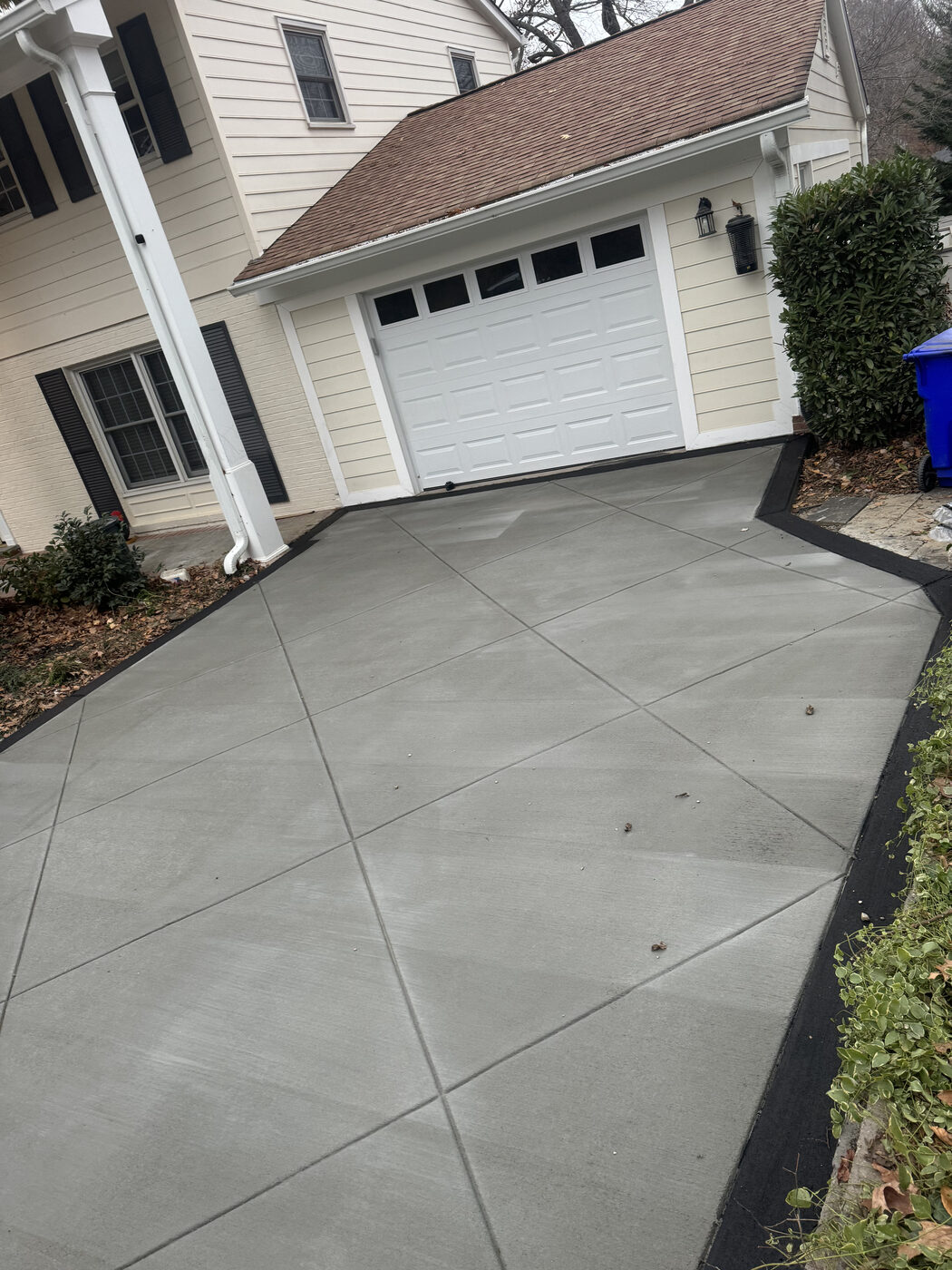 Clean single-car concrete driveway with landscaping