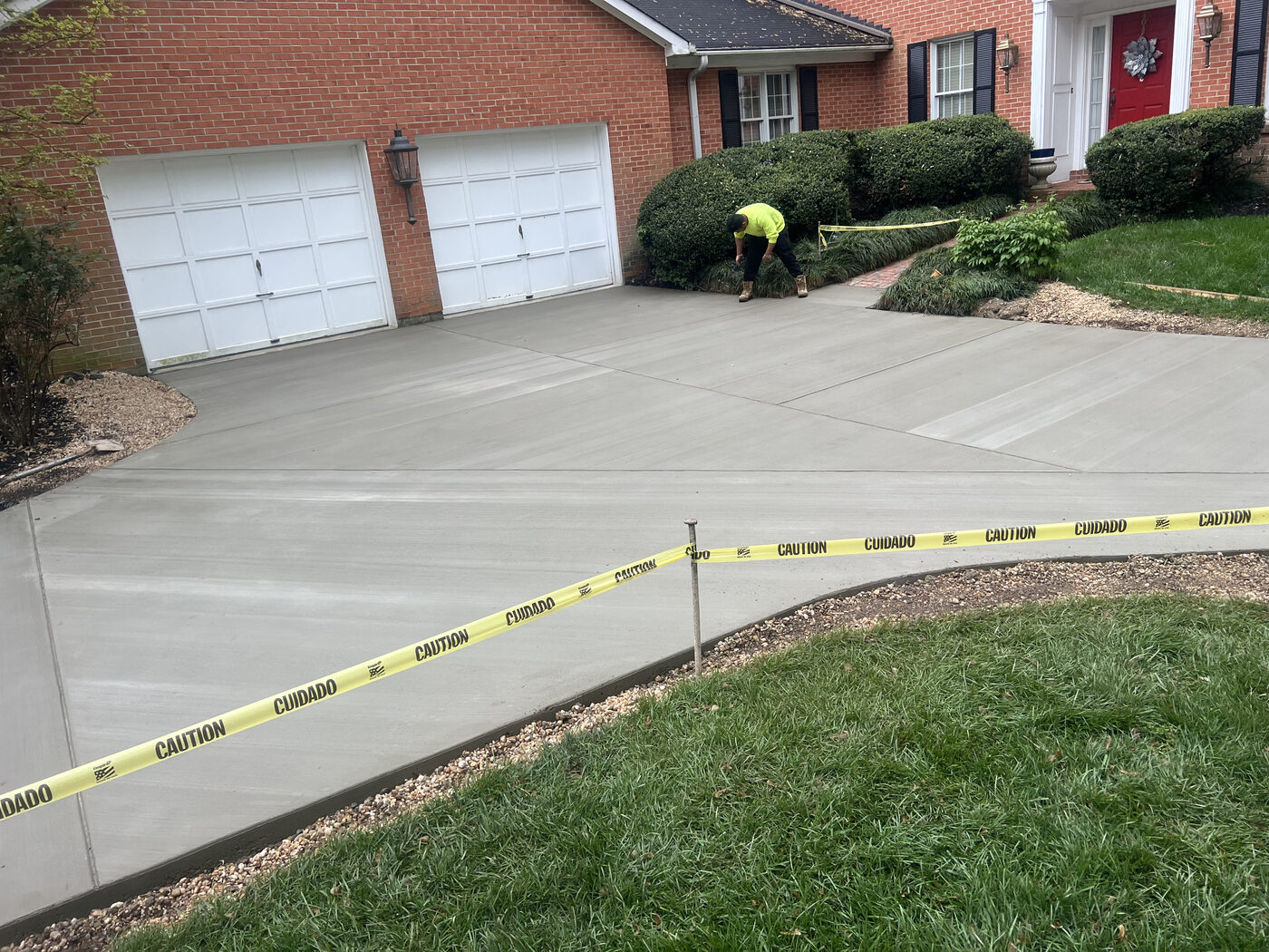 Two-car garage driveway at a brick home with crew finishing edges