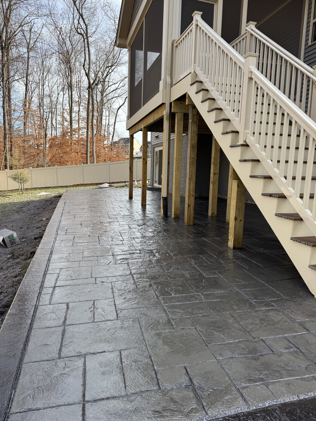 Stamped tile-pattern concrete patio beneath a deck staircase