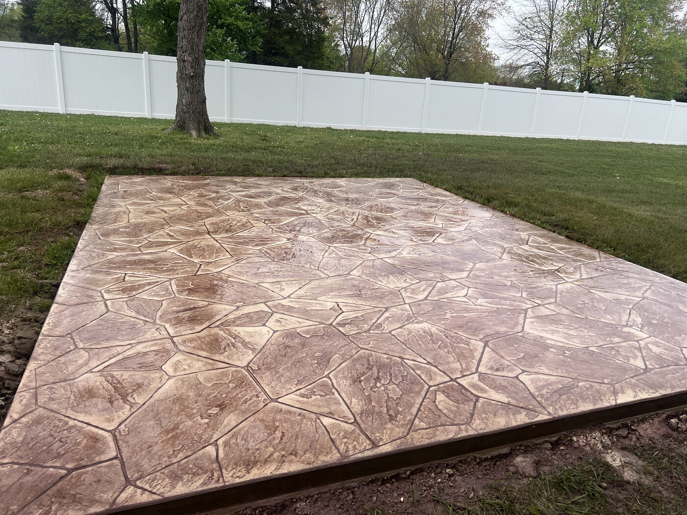 Large stamped stone-pattern patio with a white vinyl fence